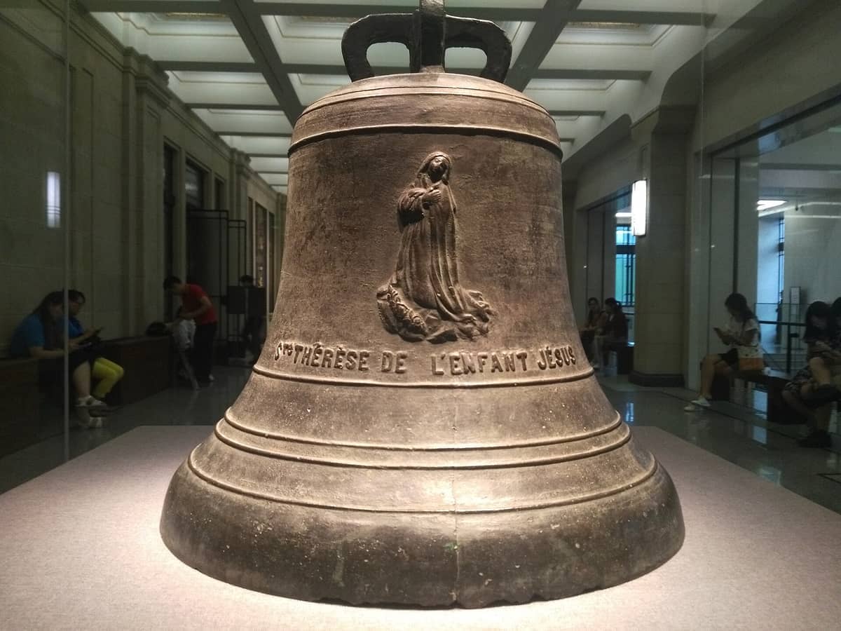 Große historische Bronzeglocke mit Inschrift und religiöser Figur im Shanghai History Museum ausgestellt, mit Besuchern, die entlang der Galeriewände sitzen.