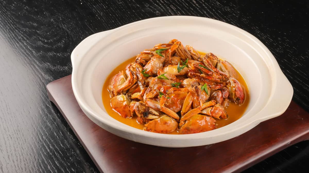 Potongan kepiting berbulu kukus yang disusun dalam mangkuk tanah liat putih, khas masakan musim gugur Shanghai, di atas meja gelap.
