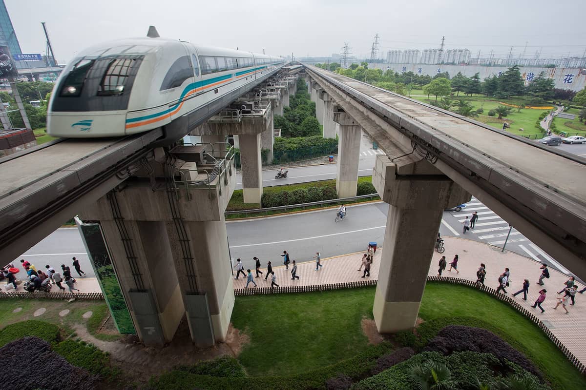 Die Shanghaier Magnetschwebebahn fährt mit hoher Geschwindigkeit auf ihrer erhöhten Trasse, darunter Menschen und Straßenverkehr – ein Blick auf den modernen Zug und seine einzigartige Infrastruktur.
