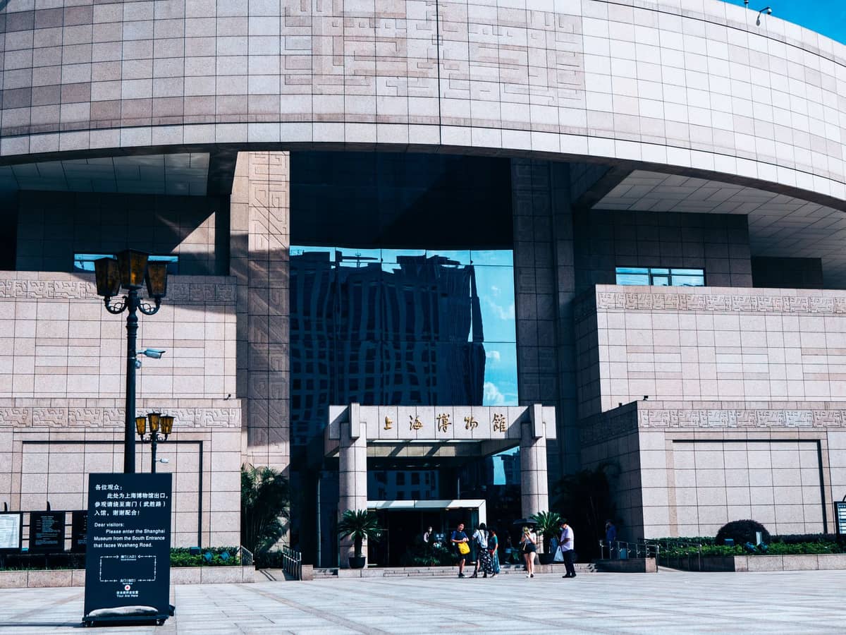 Der Haupteingang des Shanghai Museums mit seiner markanten runden Architektur, der steinernen Fassade und Besuchern, die an einem sonnigen Tag eintreten.