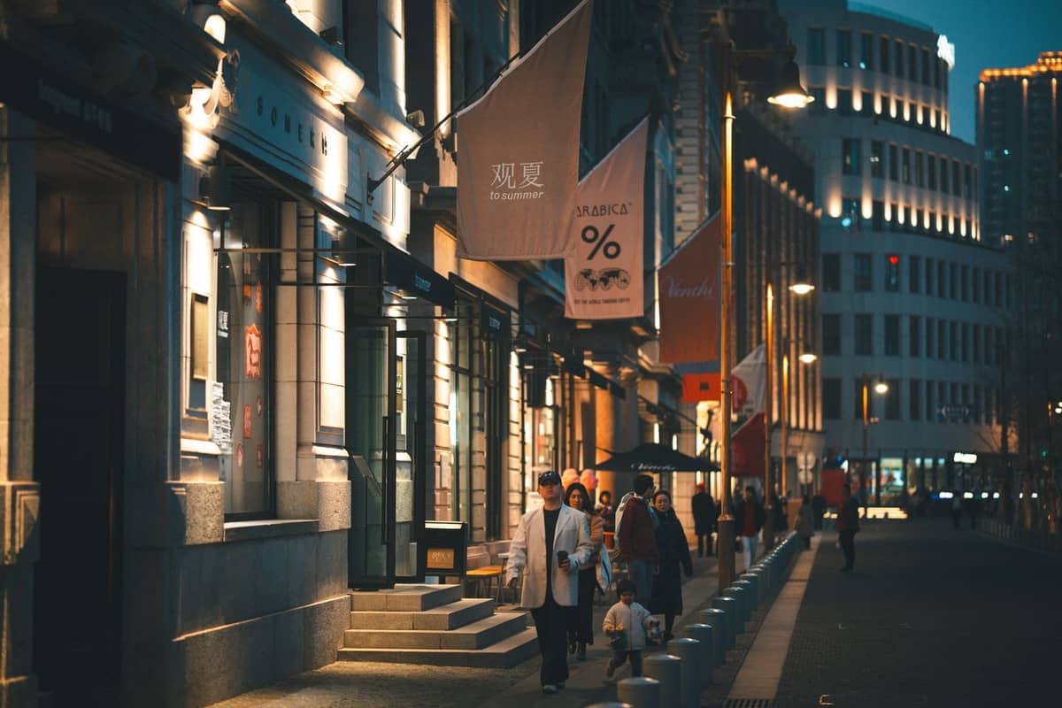 Scène nocturne avec des personnes se promenant dans une rue chaleureusement éclairée bordée de bâtiments historiques et d'enseignes de bars à Shanghai.