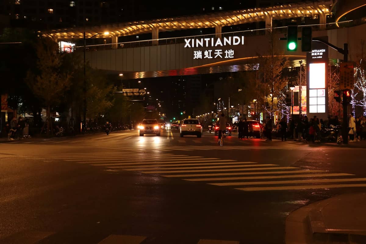 Scène de rue nocturne à Xintiandi, Shanghai, avec une enseigne illuminée, des voitures et des personnes dans un quartier animé de vie nocturne.