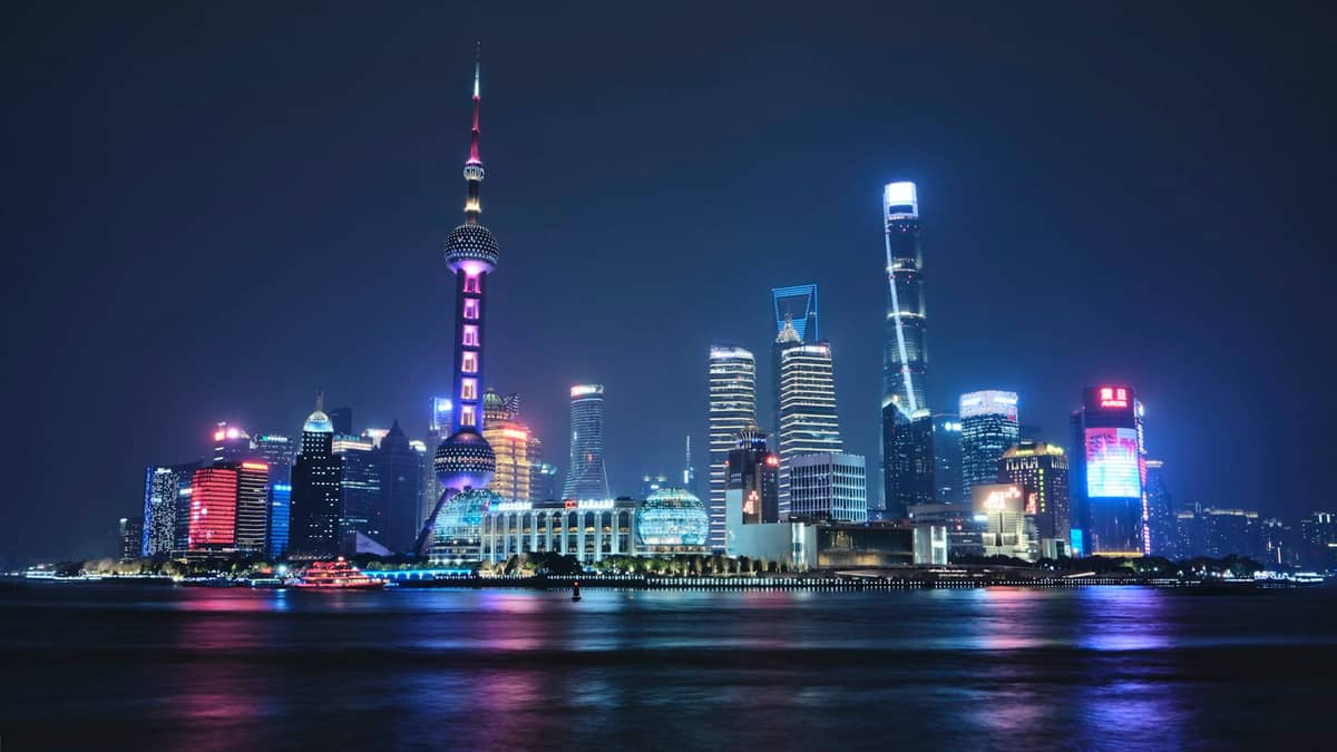 La skyline illuminée de Pudong à Shanghai la nuit vue depuis l'autre rive du fleuve, mettant en valeur l'Oriental Pearl Tower et la Shanghai Tower.