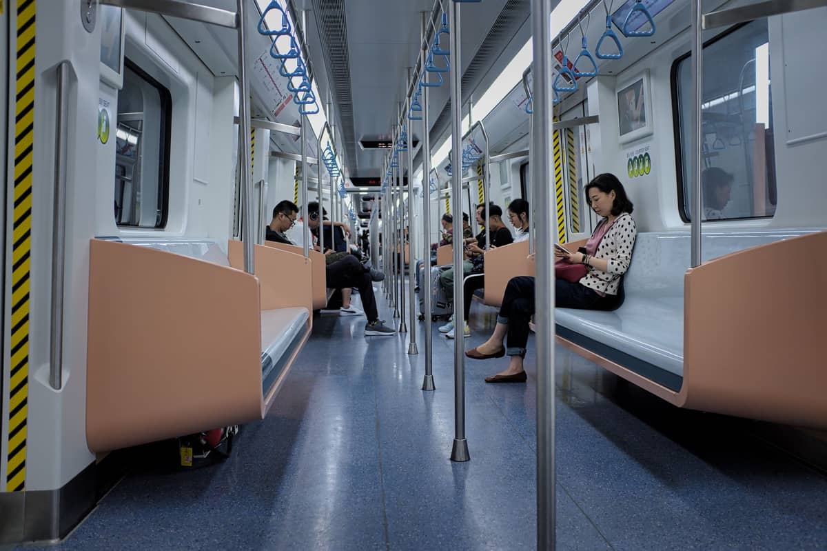 Des passagers assis à l'intérieur d'une rame moderne du métro de Shanghai avec des sols bleus et des sièges orange.