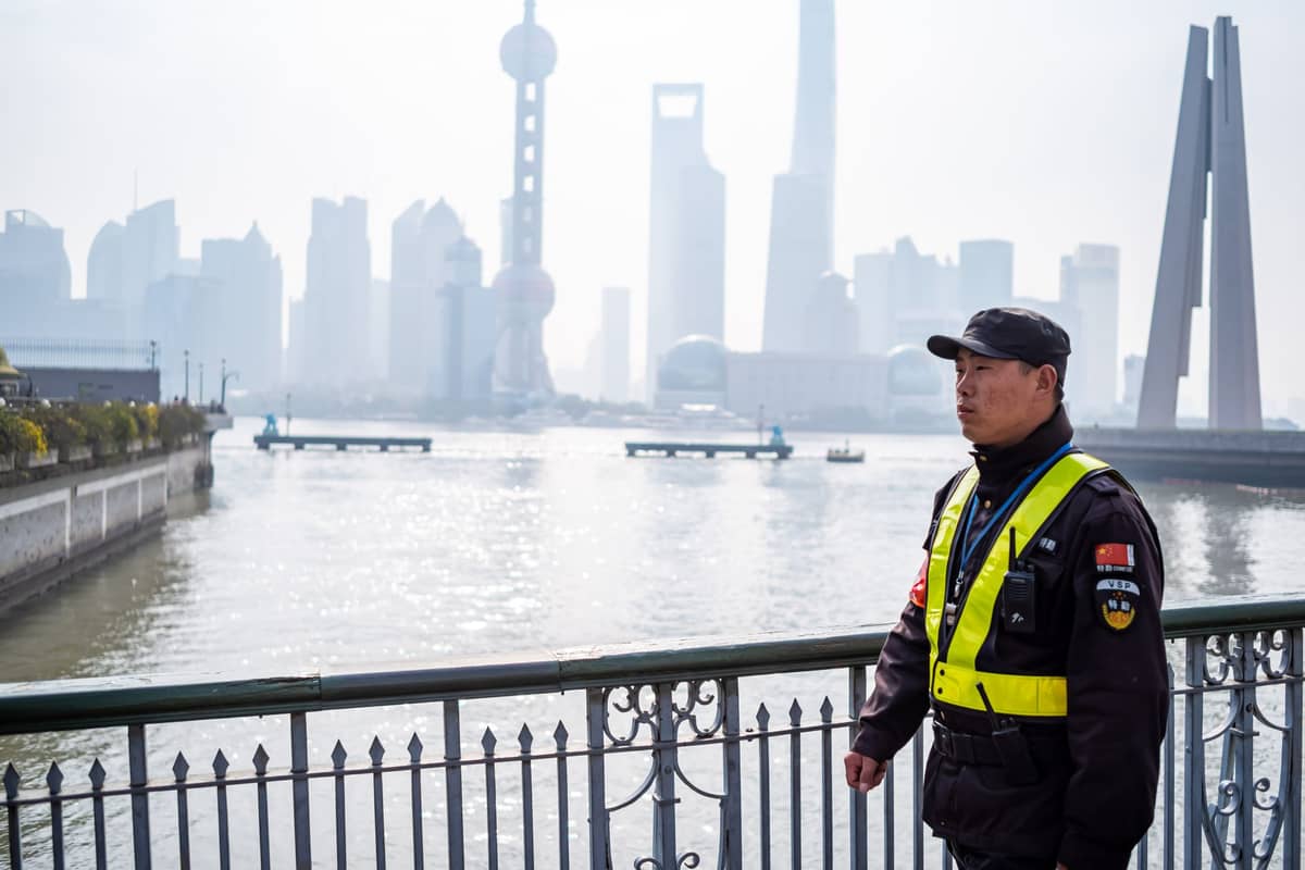 Ein uniformierter Sicherheitsbeamter steht an einem Geländer mit Blick auf den Huangpu-Fluss – dahinter die ikonische Shanghaier Skyline mit dem Oriental Pearl Tower.