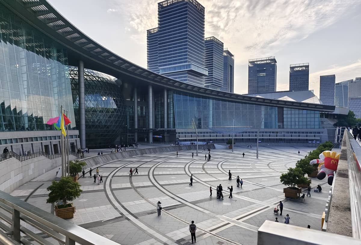 Weitwinkelperspektive auf den Außenbereich des Shanghai Science and Technology Museum mit seiner markanten Glasdom-Fassade, der geschwungenen modernen Architektur und Besuchern auf dem weitläufigen Vorplatz.