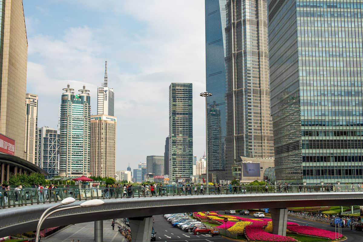 Modern skyscrapers and elevated pedestrian walkway in Lujiazui, Pudong, Shanghai, with visible shopping malls and busy street below.