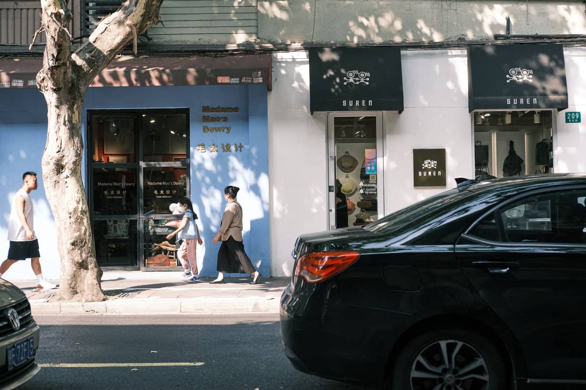 Pedestrians walking along a boutique retail street in Shanghai’s Former French Concession, with small independent shops and cafes under leafy trees.