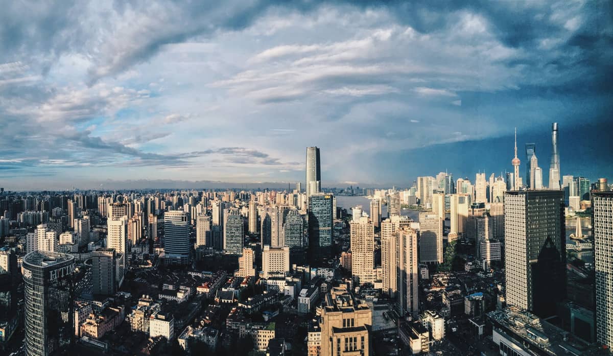 Wide panoramic view of Shanghai cityscape with dense high-rise buildings and iconic skyline under dramatic sky, illustrating the city's vast urban scale.