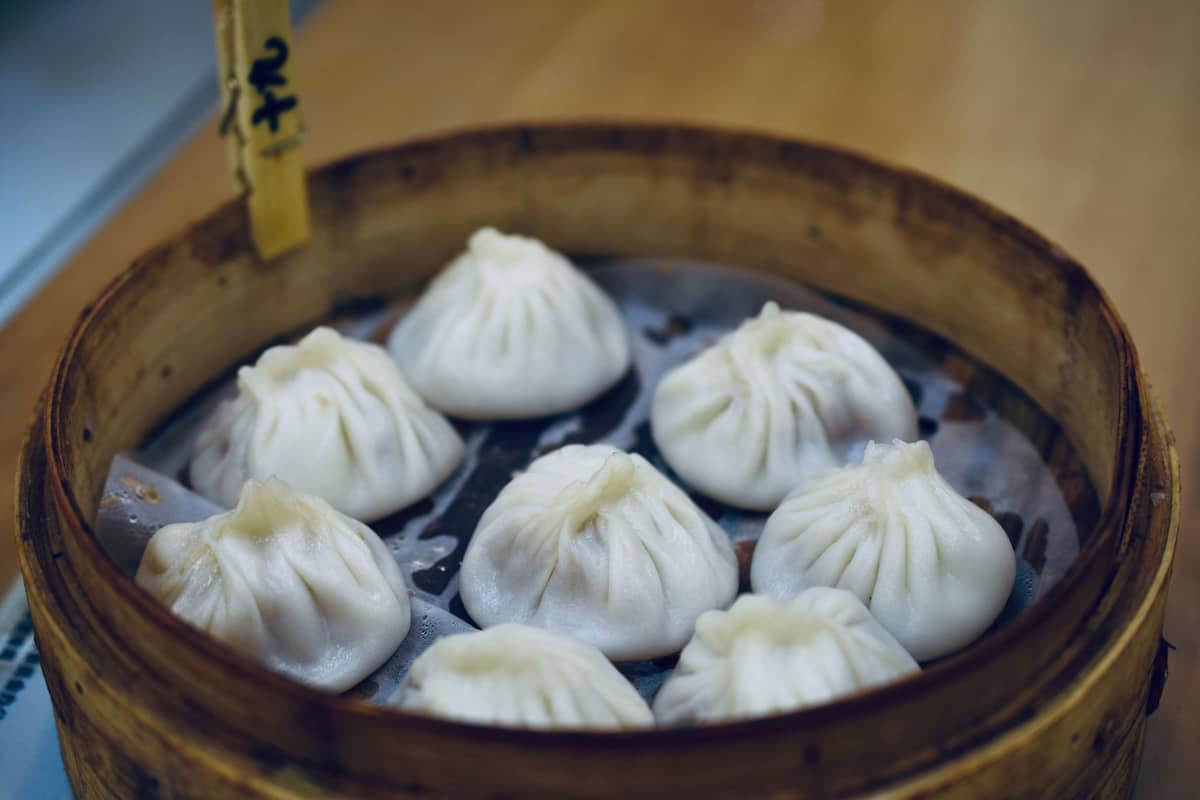 Ein Bambusdämpfer voller frisch gedämpfter Shanghaiiner Suppendumplings (Xiaolongbao) auf einem Tisch, mit ihrer charakteristischen dünnen, gefältelten Teighülle.