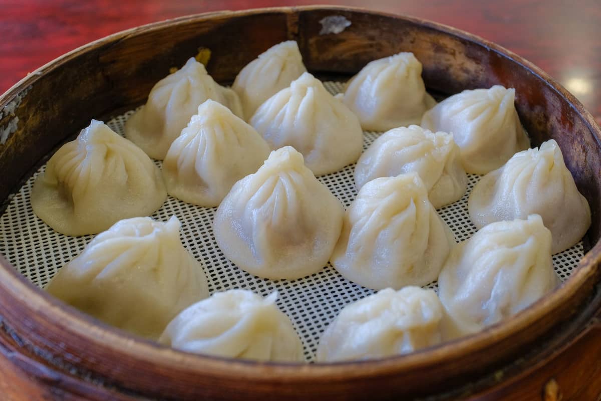 Ein Bambus-Dämpfkorb gefüllt mit vielen Xiaolongbao auf einem Restauranttisch.