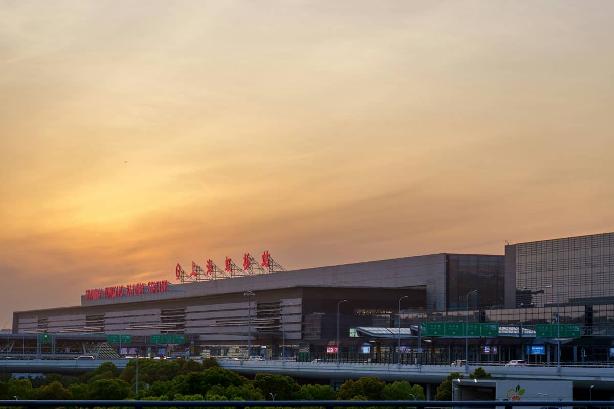 Außenansicht des Flughafenterminals Shanghai bei Sonnenuntergang mit chinesischen Schriftzeichen auf dem Dach und Autobahn davor