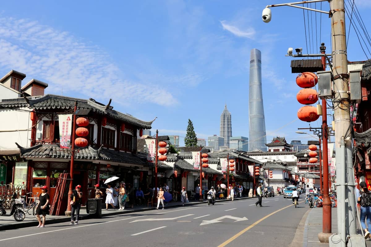Traditionelle chinesische Gebäude mit roten Laternen in einer belebten Straße in Shanghais Altstadt, mit dem modernen Shanghai Tower im Hintergrund.