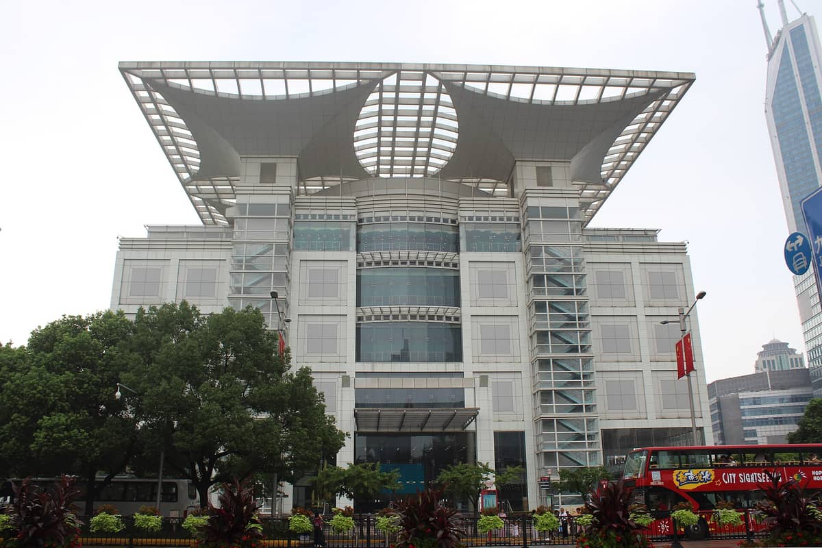 Außenansicht des Shanghai Stadtplanungsausstellungszentrums mit seinem markanten Dachdesign, vom Straßenniveau aus gesehen, mit Bäumen und Menschen davor.