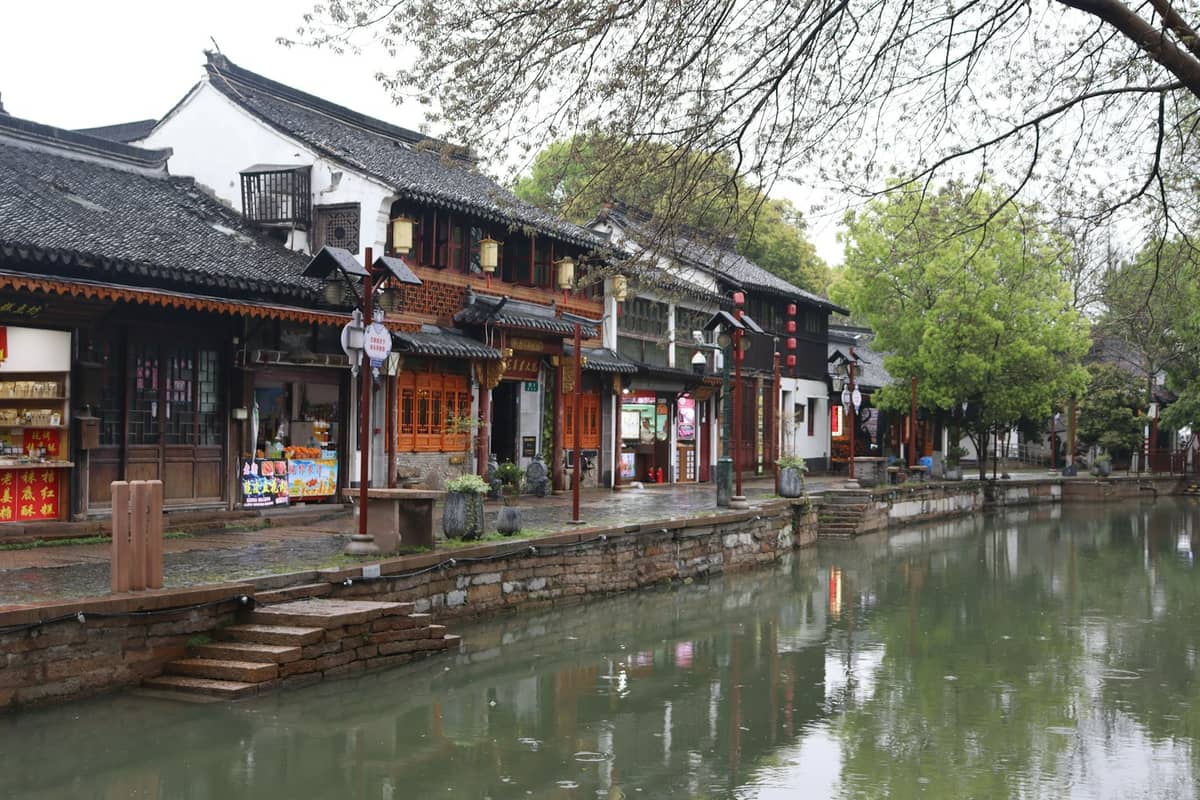 Traditional buildings with shops beside a canal in a classic Shanghai water town, green trees and clear spring weather reflected on the water.