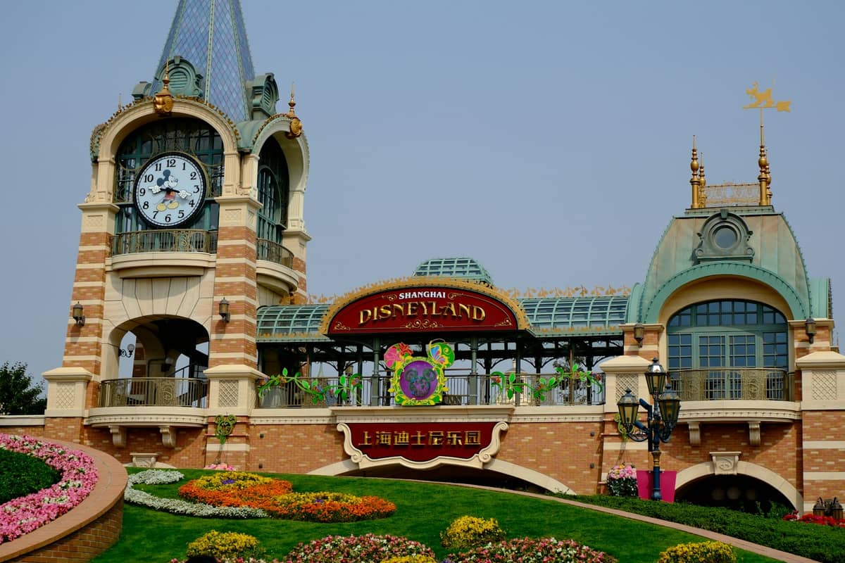 Pintu masuk dan menara jam Shanghai Disneyland, dengan dekorasi bunga dan tanda resmi taman dalam bahasa Inggris dan Mandarin.