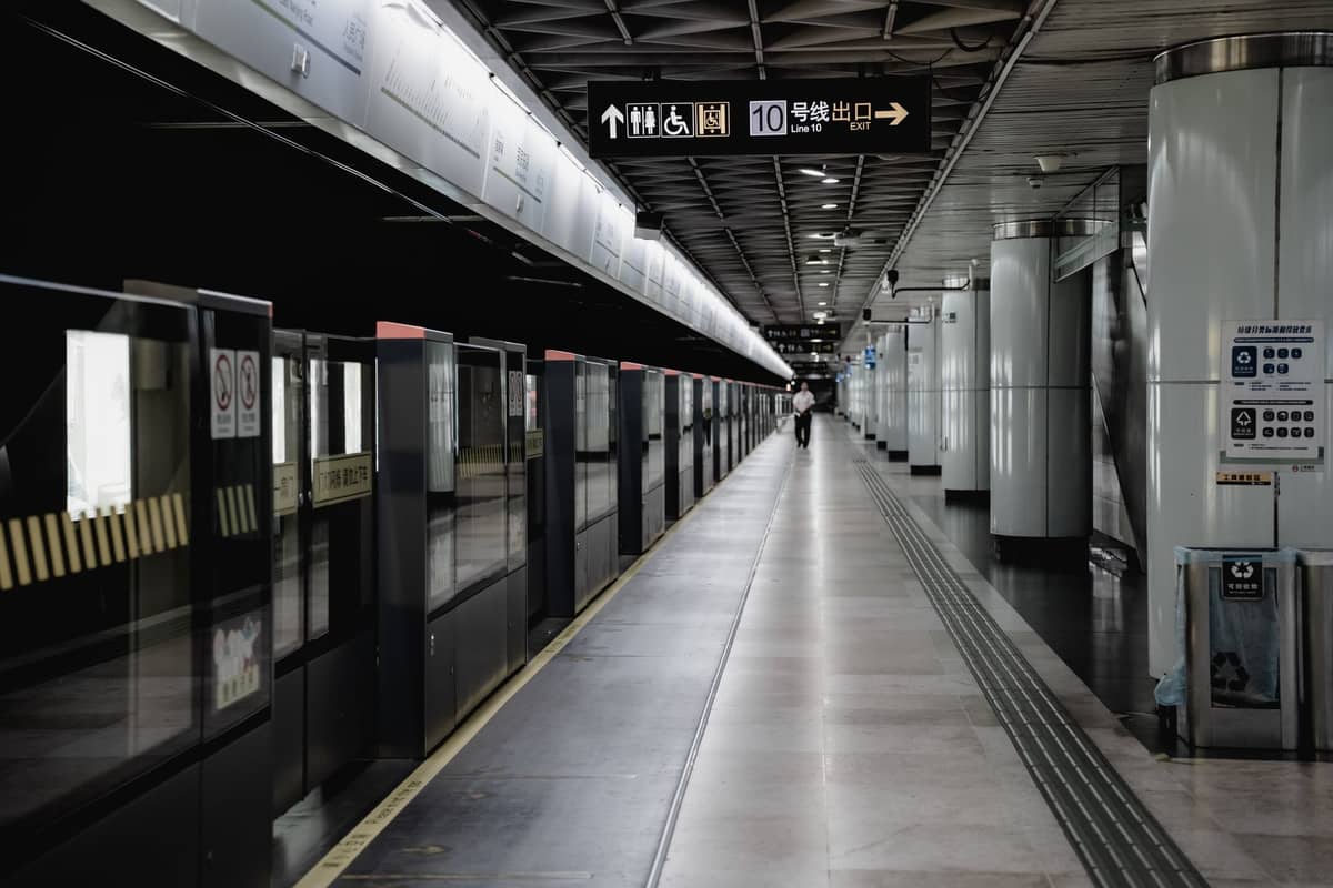 Peron stasiun metro modern di Shanghai dengan penghalang keamanan kaca, papan petunjuk bilingual, dan koridor yang aksesibel, dengan seseorang di kejauhan.