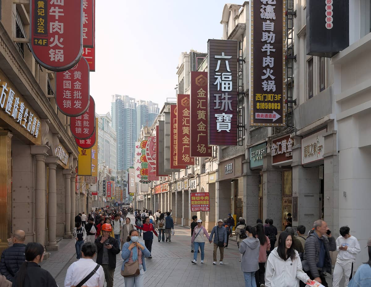 Crowded pedestrian street in Guangzhou’s Shangxiajiu with historic Lingnan shophouses, numerous hanging red shop signs, and people walking along the busy commercial strip.