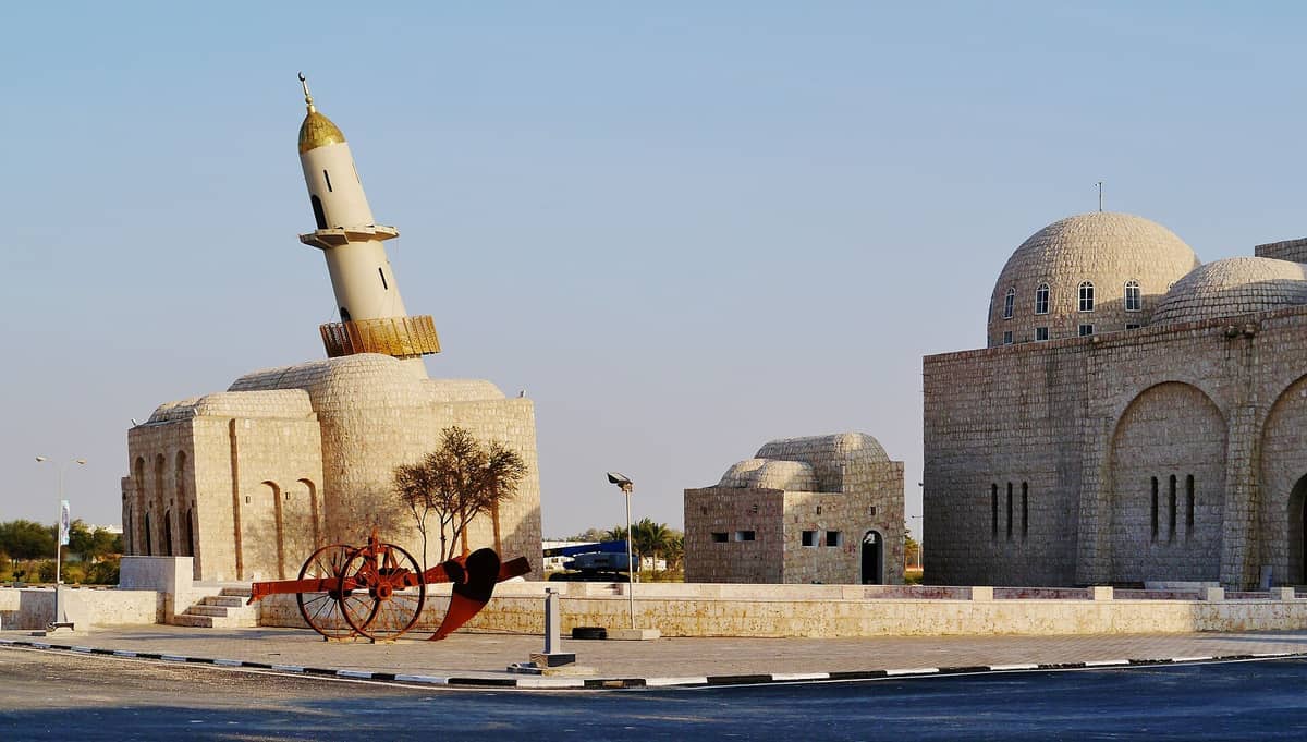 Sandfarbene Steingebäude mit Kuppeldächern und einem schiefen Minarett im Sheikh Faisal Bin Qassim Al Thani Museum unter klarem blauem Himmel.