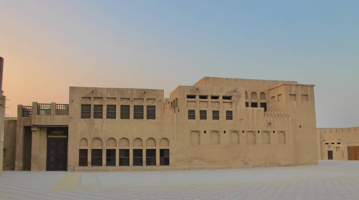 Weitwinkelpanorama des Sheikh Saeed Al Maktoum House bei Sonnenuntergang mit der vollständigen sandfarben Fassade und den traditionellen Bogenfenstern des Erbe-Gebäudes in Dubai.