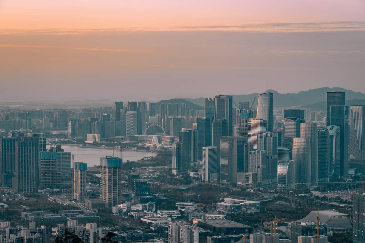 Vista aérea ampla do horizonte de Shenzhen ao pôr do sol, mostrando arranha-céus densos e um moderno traçado urbano com montanhas ao fundo.