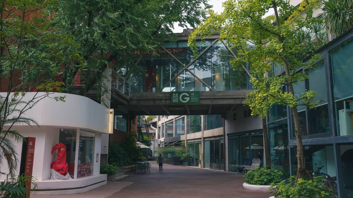 Um distrito artístico para pedestres no OCT-LOFT de Shenzhen, com galerias modernas, caminhos arborizados, edifícios com fachadas de vidro e uma escultura de arte pública visível.