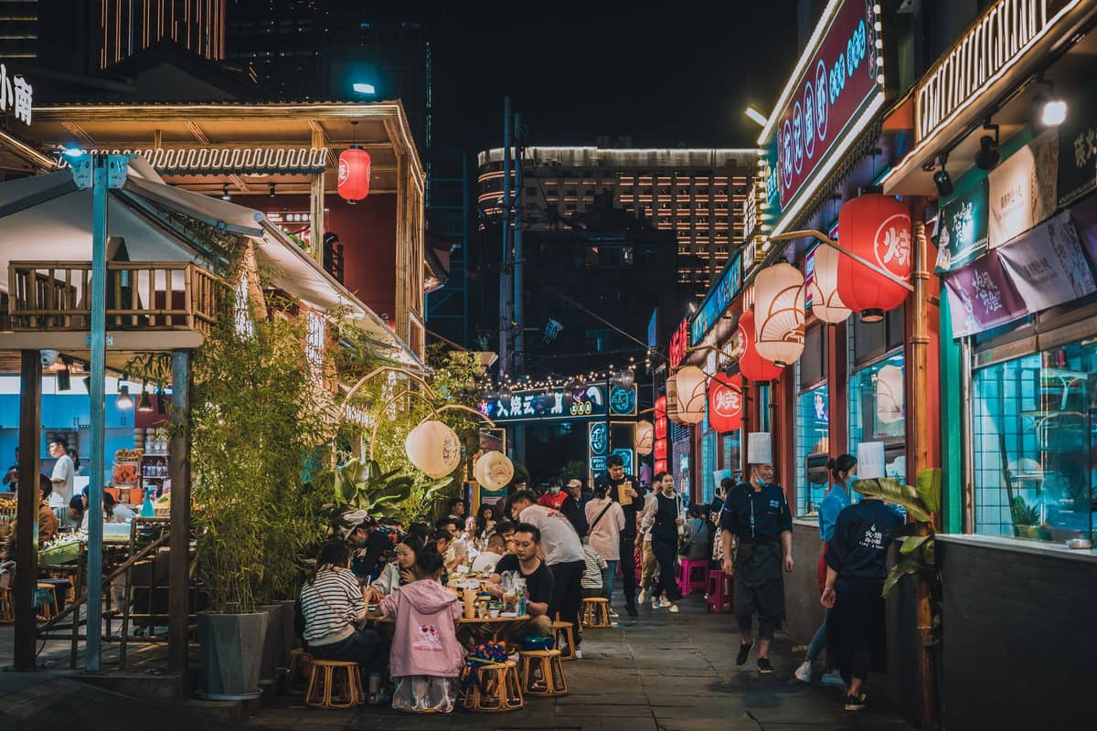 Movimentada rua de comida noturna em Shenzhen com jantares ao ar livre, lanternas tradicionais e restaurantes lotados, destacando os bairros gastronômicos locais.