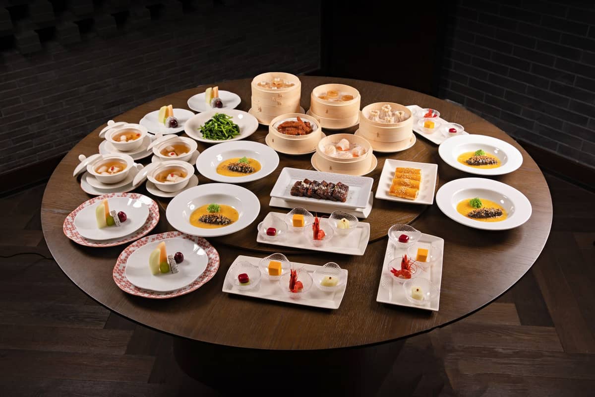 Uma mesa redonda servida com pratos ao estilo cantonês, incluindo dim sum, pães cozidos a vapor, sopas, legumes cozidos a vapor e sobremesas tradicionais.