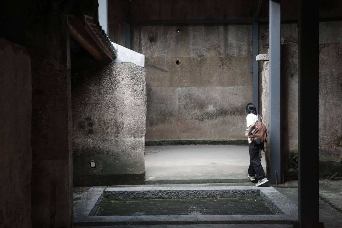 Um viajante com mochila explora o pátio interno de uma antiga fortaleza de pedra em Shenzhen, revelando uma arquitetura histórica escondida além dos pontos turísticos convencionais.