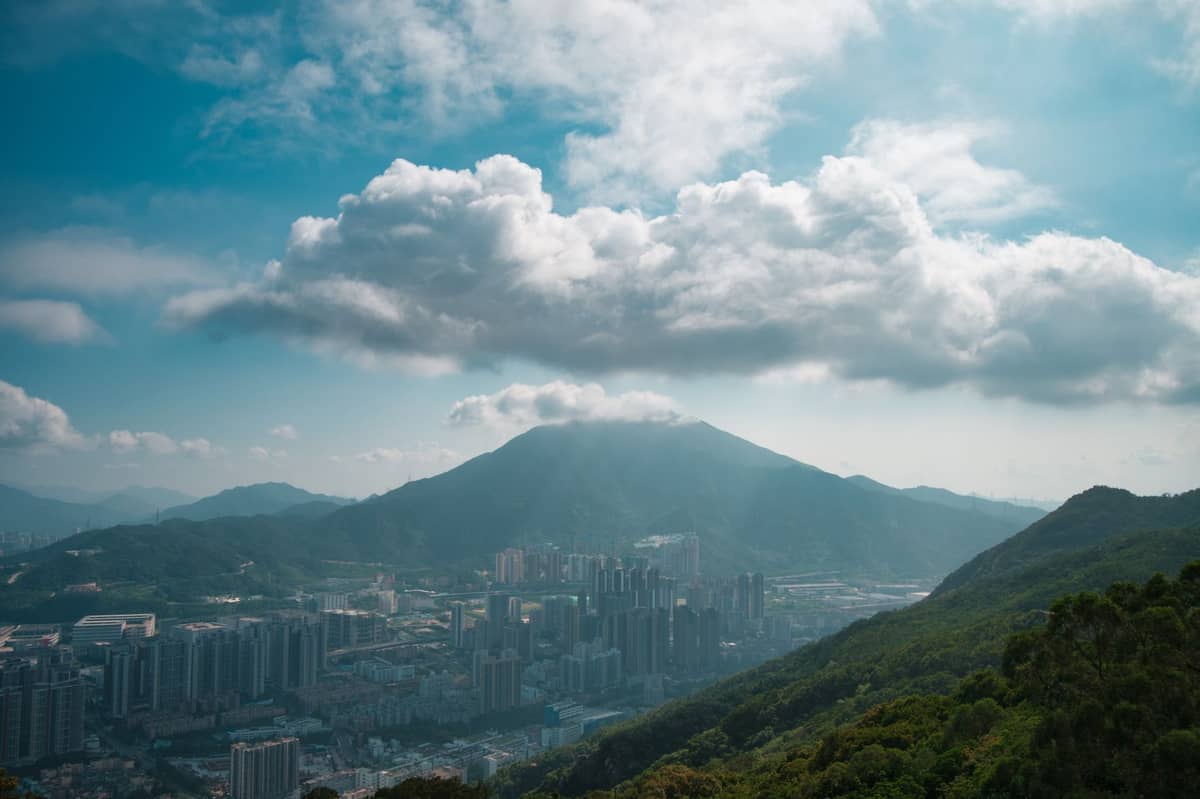 Horizonte urbano com edifícios densamente agrupados ao pé de uma montanha proeminente coberta de exuberante vegetação verde sob um céu azul.