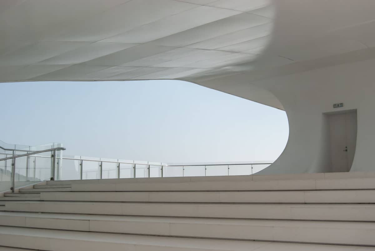 Vista panorâmica do interior arquitetônico branco, curvilíneo e futurista do Museu de História Natural de Shenzhen, com escadarias elegantes e grandes aberturas de janelas.