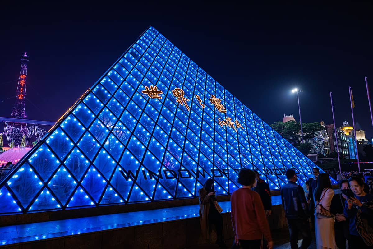 Multidões se reúnem perto da iluminada entrada em pirâmide azul do parque temático Window of the World de Shenzhen, uma popular atração paga à noite.