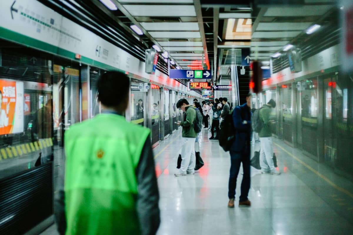 Pessoas esperando em uma moderna plataforma de metrô em Shenzhen, com sinalização clara, barreiras de vidro e um trem chegando.
