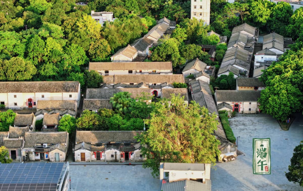 Vista aérea de uma histórica aldeia chinesa com casas tradicionais de telhados cinzentos rodeadas por vegetação exuberante, destacando o patrimônio arquitetônico em um ambiente similar a um parque.