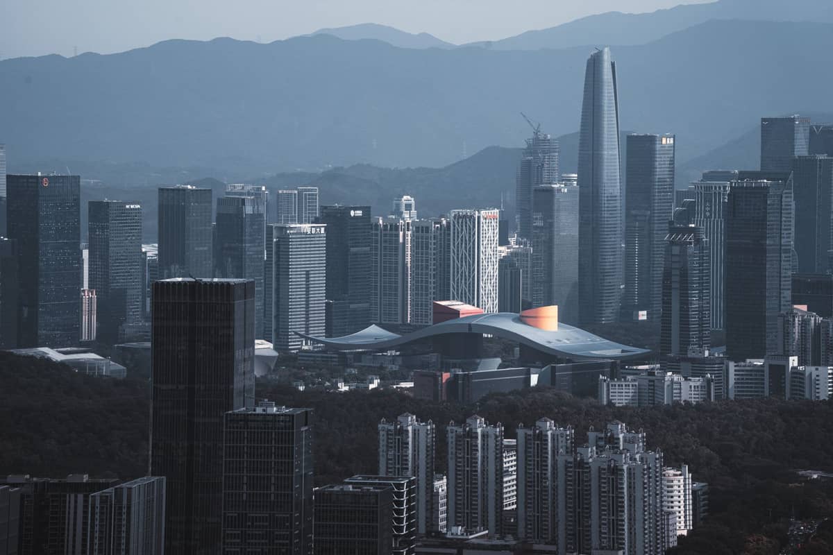 Vista panorâmica do skyline de Shenzhen com o icônico Civic Center e o Ping An International Finance Centre ao fundo de montanhas no entardecer.
