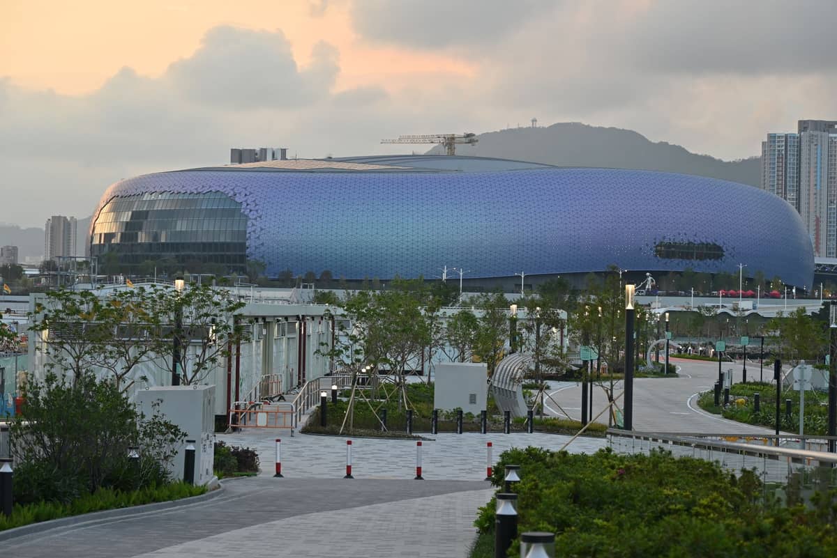 Edifício arredondado moderno e distinto com azulejos roxos do Shenzhen Natural History Museum com um caminho ajardinado e edifícios da cidade ao fundo.