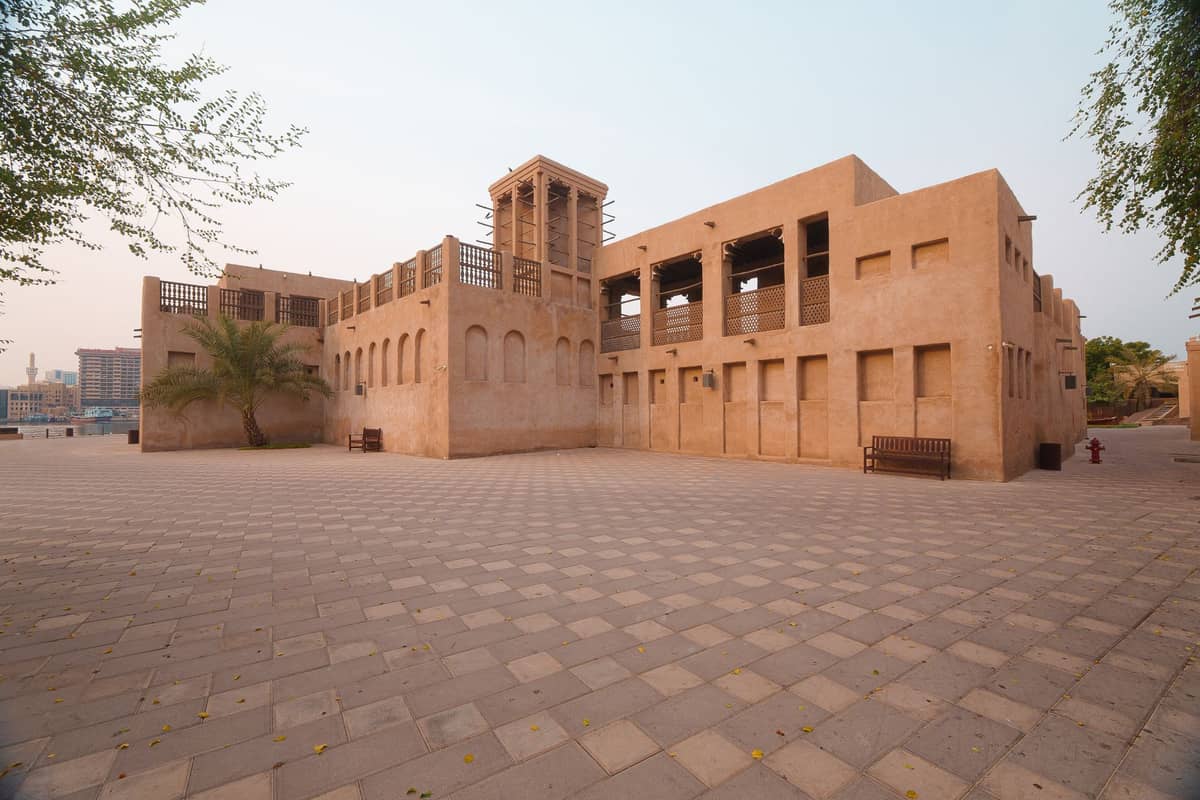 Restaurierte historische Gebäude des Al Shindagha Heritage District in Dubai mit Windtürmen und traditioneller Golfarchitektur neben einer weitläufigen Steinpromenade.