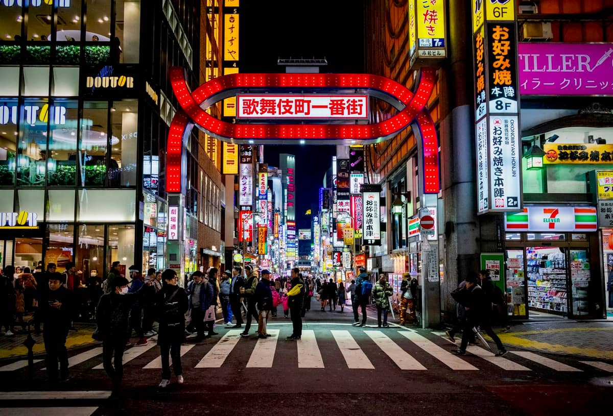 Entrance to Kabukicho in Shinjuku at night, with large illuminated red sign over the street, neon lights, and many people crossing the road.