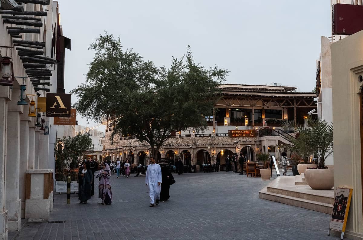 Souq Waqif in Doha mit traditioneller Architektur, Bogengängen, flanierenden Menschen und lebhafter Marktatmosphäre in der Abenddämmerung.