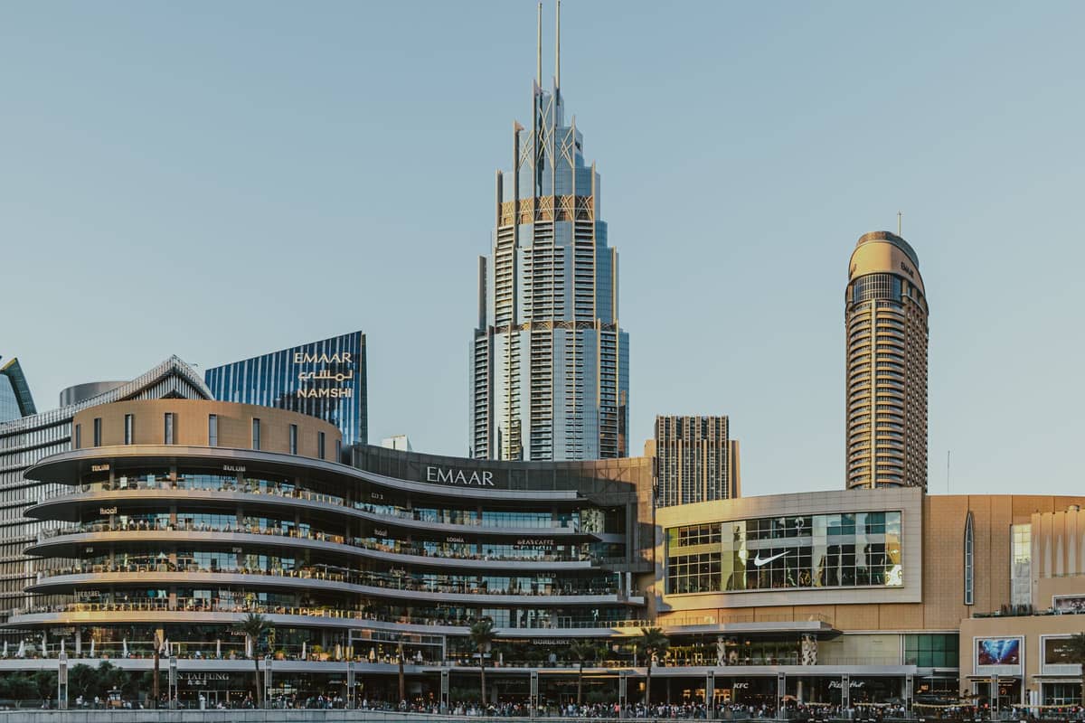 Tagesansicht des Außenbereichs der Dubai Mall mit Hochhäusern im Hintergrund und dem Emaar-Logo auf der Fassade des Einkaufszentrums.