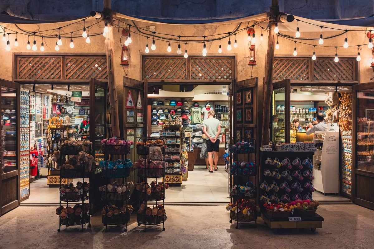 Ein gut beleuchtetes Souvenirladen in Dubai mit offenen Türen, mit bunten Geschenken und Andenken in den Regalen, unter Lichterketten bei Nacht.
