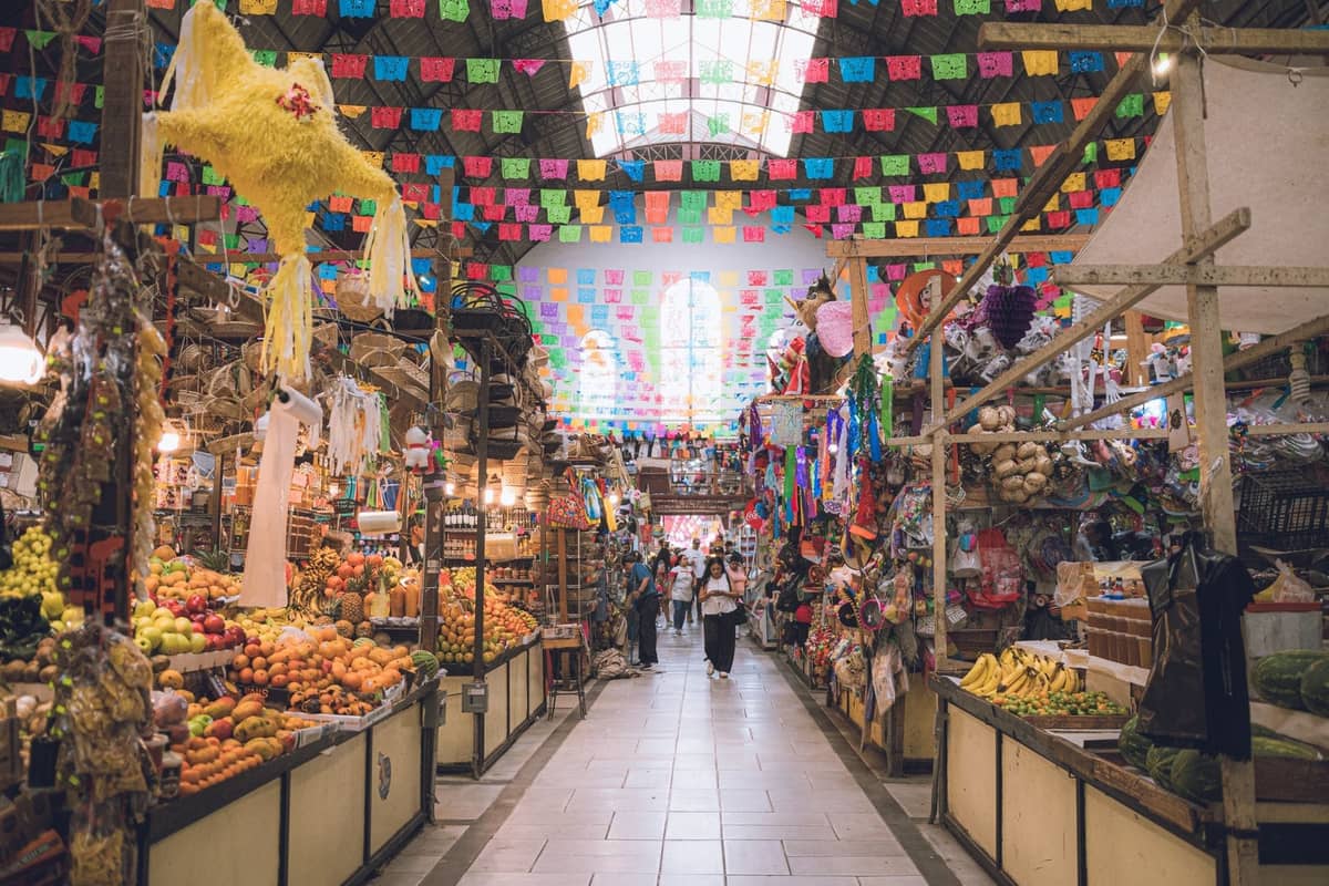Farbenfrohes Inneres des Mercado Libertad mit Ständen voller Früchte und Waren, Papel-picado-Dekorationen und durch das Dach einfallendem natürlichen Licht.