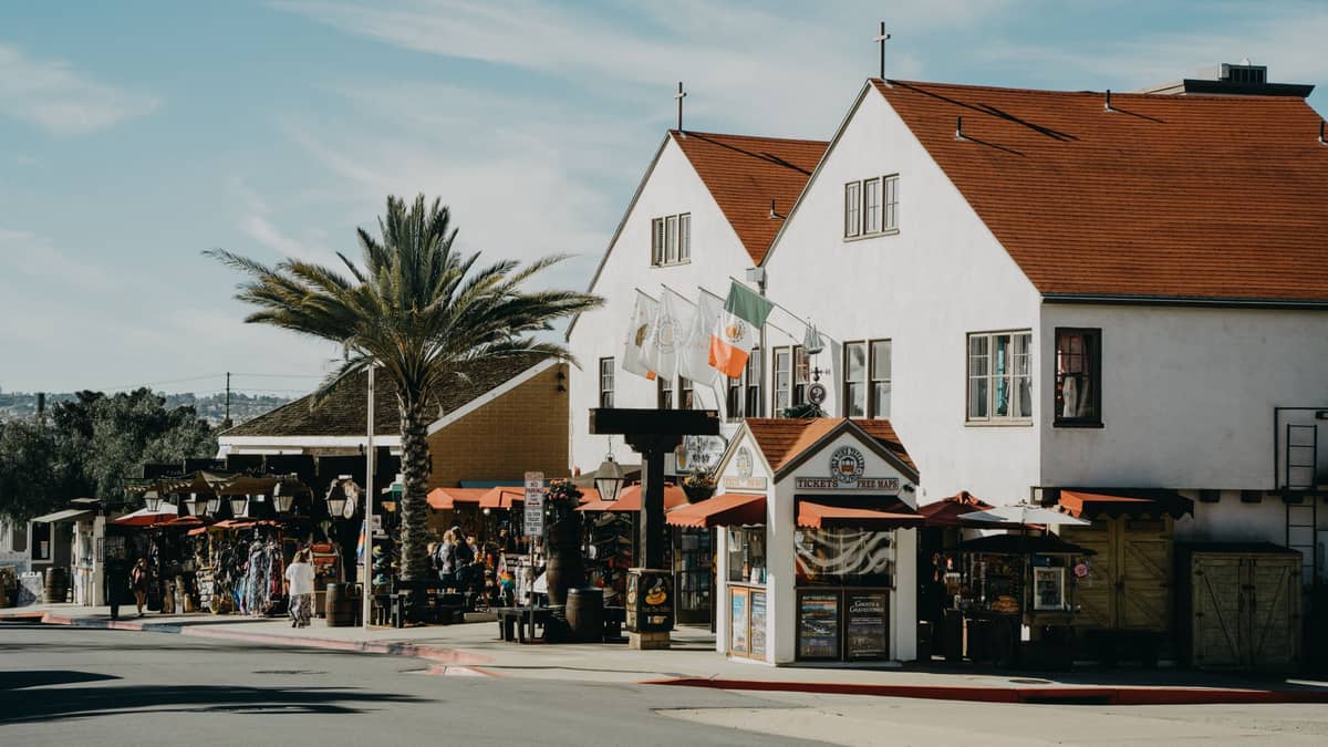 Geschäfte und Boutiquen säumen die fußgängerfreundlichen Straßen von San Diegos Old Town, mit Palmen, Außenauslagen und Fahnen über weißen Stuckgebäuden.