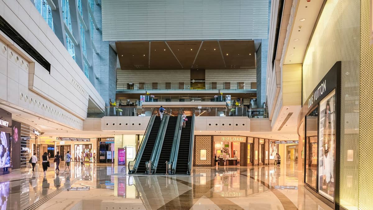 Interior amplo e iluminado de um shopping center em Seul com escadas rolantes, fachadas de lojas de luxo e pisos polidos, visto a partir da área central do shopping.