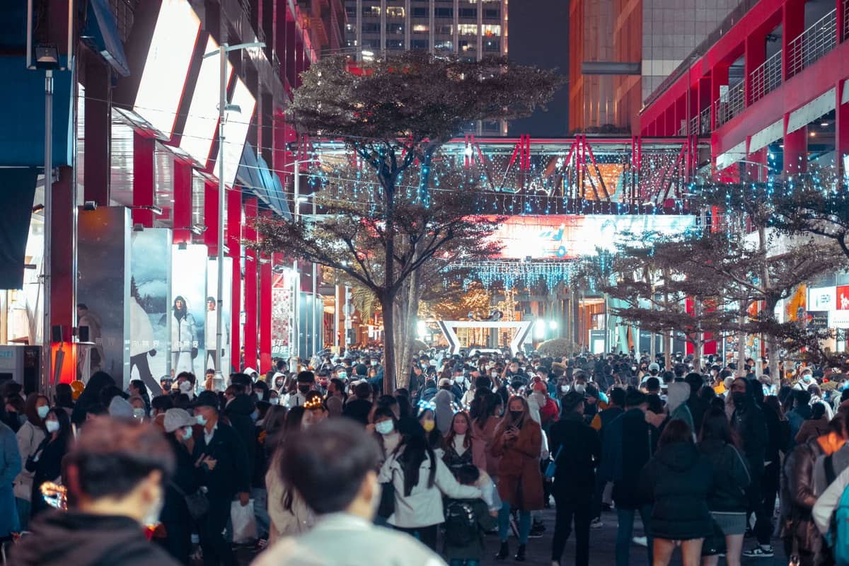 Movimentada rua comercial para pedestres, bem iluminada à noite, ladeada por lojas modernas e repleta de compradores locais em roupas de inverno.