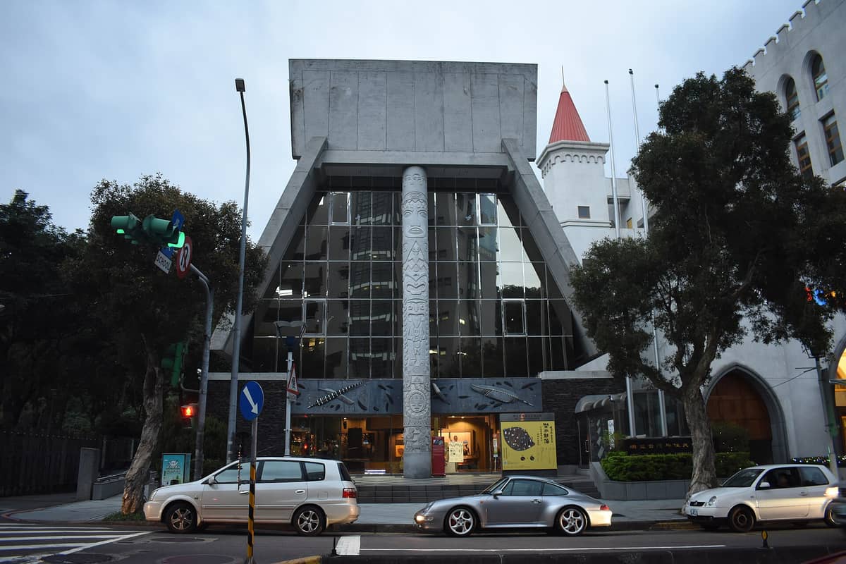Außenansicht des Shung Ye Museum of Formosan Aborigines in Taipeh mit der markanten modernen Fassade, einem großen zentralen Totempfahl und verspiegeltem Glas.