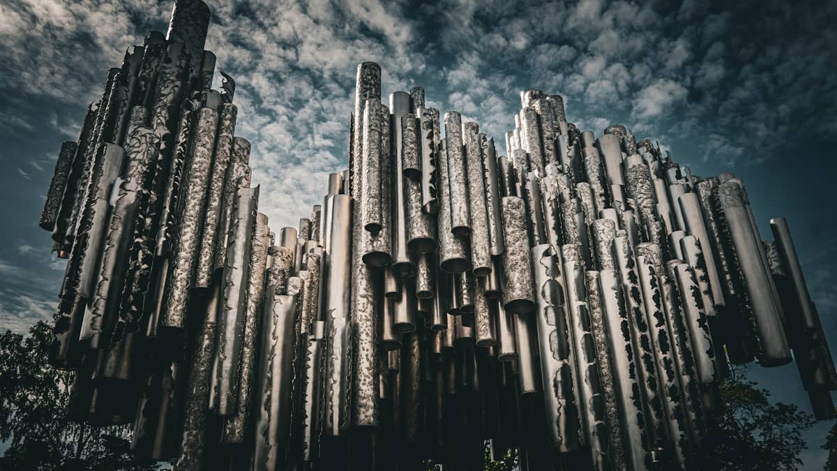 Vista de perto do Monumento a Sibelius, com seus tubos de aço inoxidável sob um céu nublado de Helsinque, destacando a forma característica em onda da escultura.