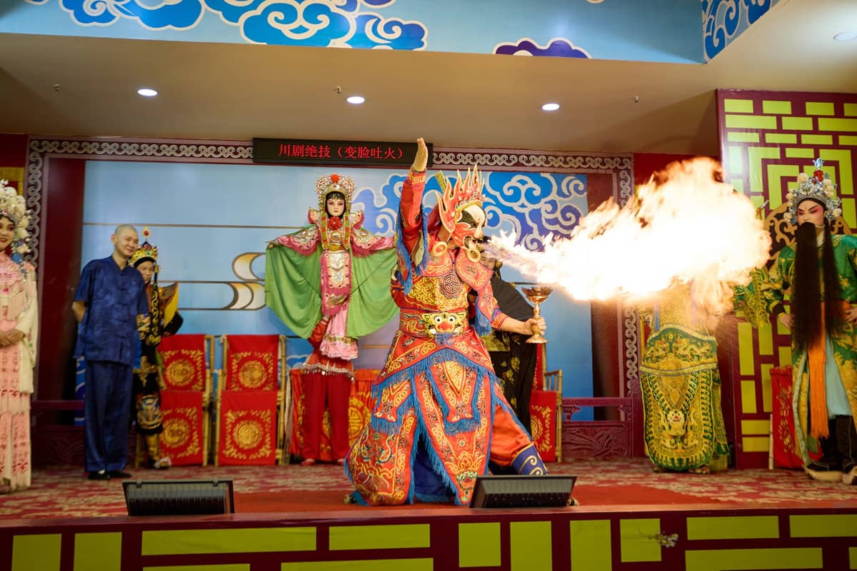Sichuan Opera performers on stage in elaborate costumes with one artist breathing fire, capturing a dramatic moment from a Chengdu opera show.