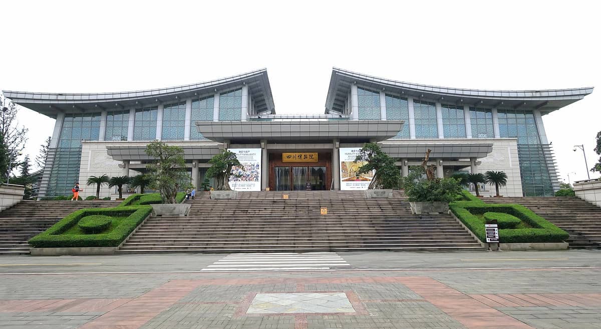 ด้านหน้าของ Sichuan Provincial Museum พร้อมด้วยผนังกระจกสมัยใหม่ บันไดหินกว้าง พุ่มไม้ที่ตัดแต่งอย่างเรียบร้อย และผู้คนบางส่วนใกล้ทางเข้า