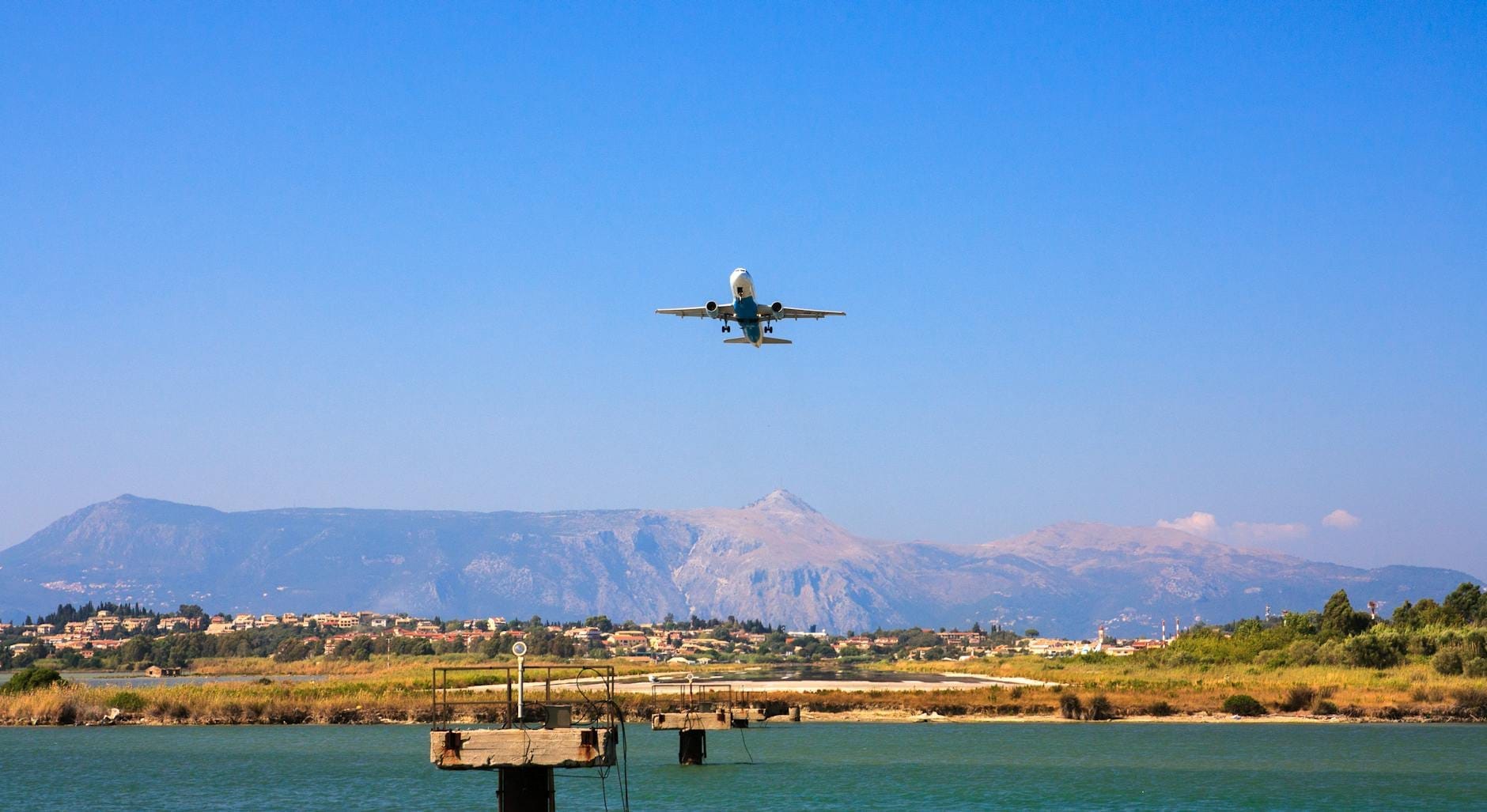 Ein Flugzeug im Landeanflug über dem Meer, im Hintergrund die sizilianische Landschaft mit Bergen und einem Dorf unter strahlend blauem Himmel.